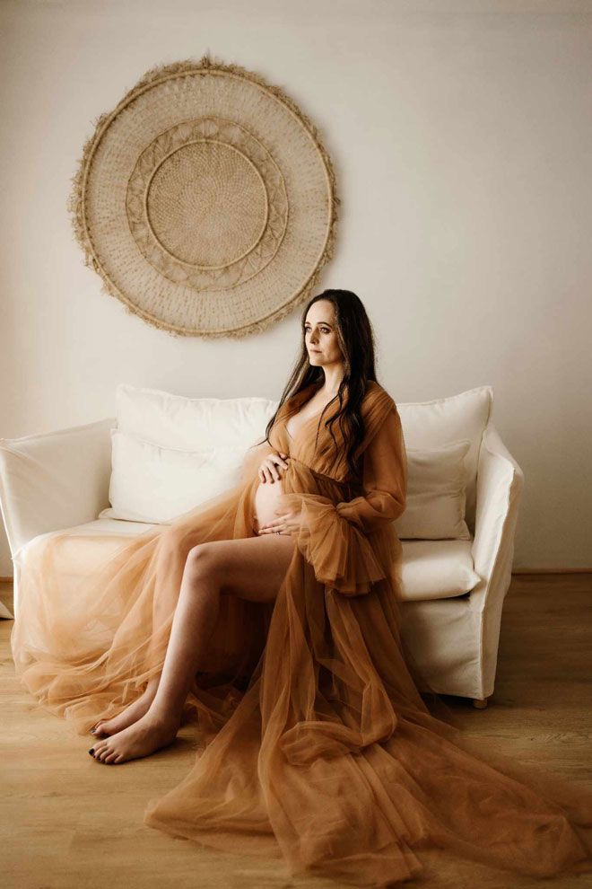 Ally in seated position with a brown dress and holding her pregnant belly
