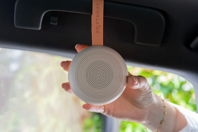 ergoPouch Driftaway white noise machine hanging in a car with woman's hand changing settings