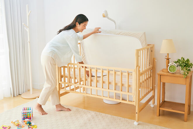 Mother installing the CuboAi Sleep Pad under a cot mattress