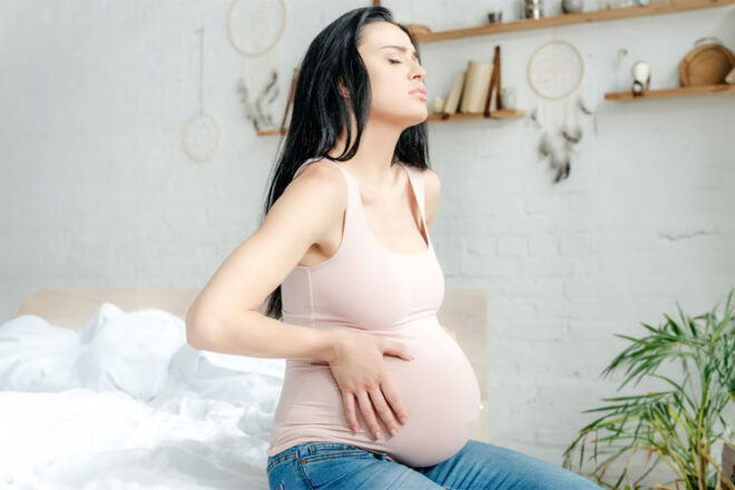 A pregnant woman looking frustrated cradling her bump