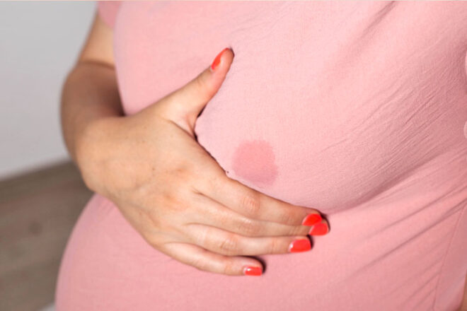 A pregnant woman holding her breast where breast milk is leaking onto her shirt