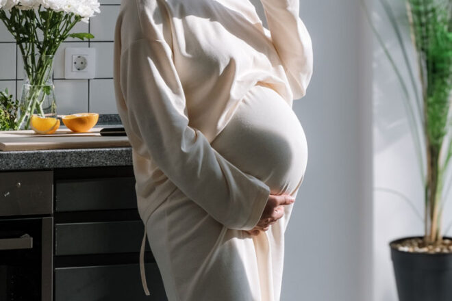A pregnant woman standing cradling her bump