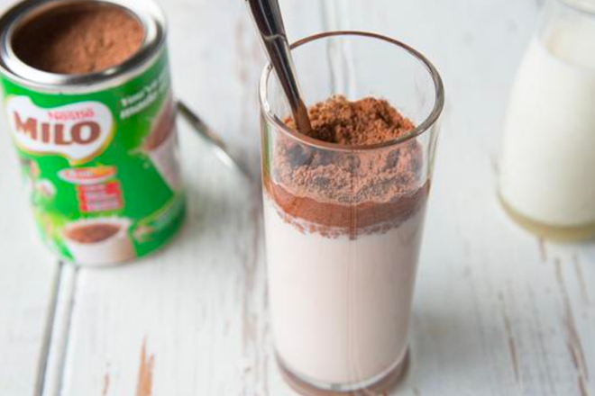 Glass of Milo milk drink with tin in background