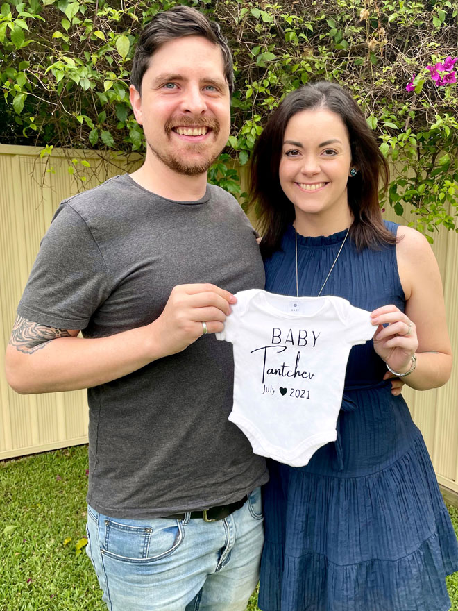 Melissa holds up a onesie for her pregnancy announcement
