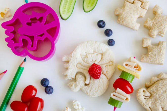 Sandwiches cut into mermaid and dinosaur shapes with the Lunch Punch sandwich cutters surrounded by food.