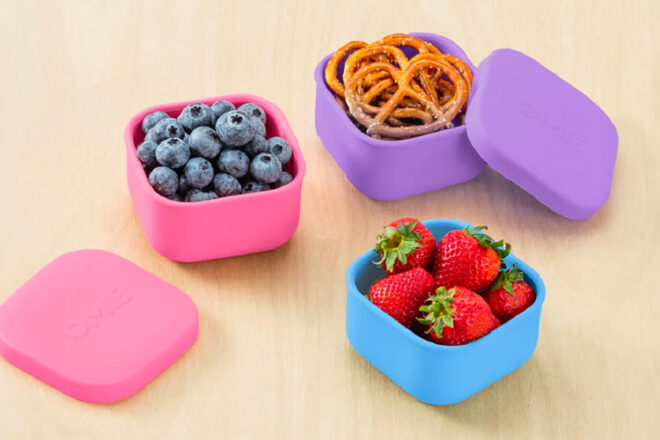 The OmieSnack Silicone Snack Boxes in pink, purple and blue filled with fruit and snack food