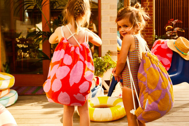 Two toddler girls carrying terry towelling swim bags from Sage & Clare