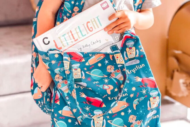 A child holding The Custom Co library bag placing a book into the bag