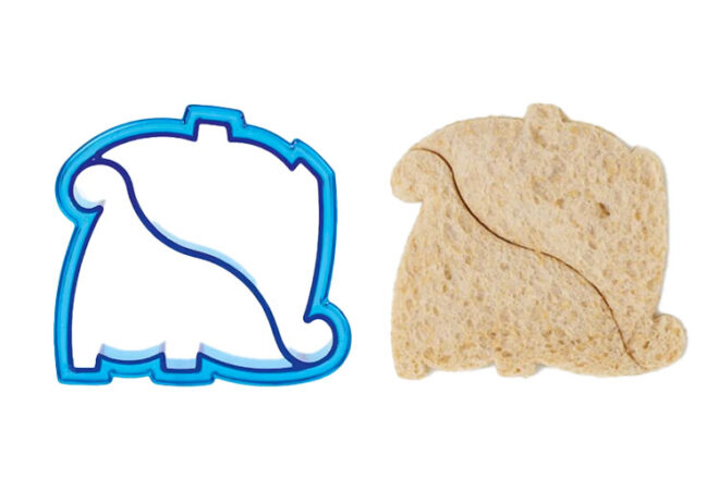 The Gingham Club double dinosaur sandwich cutter sitting next to bread that has been cut with the cutter