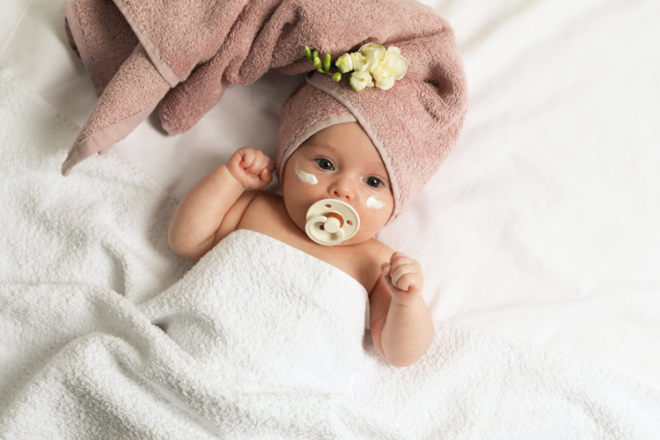 Baby with towel on head, dummy in mouth and skincare on cheeks 
