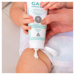 A baby sitting squeezing GAIA Baby Soothing Lotion on their leg with the help of an adult