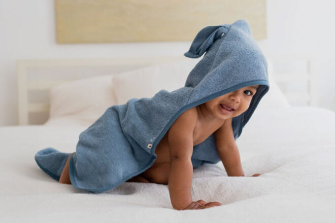 A baby on a bed wearing the BIBS Organic Hoodie Towel