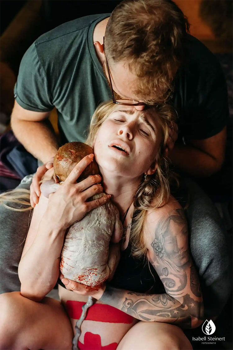 A woman being cradled by a man while she holds her newborn baby to her chest