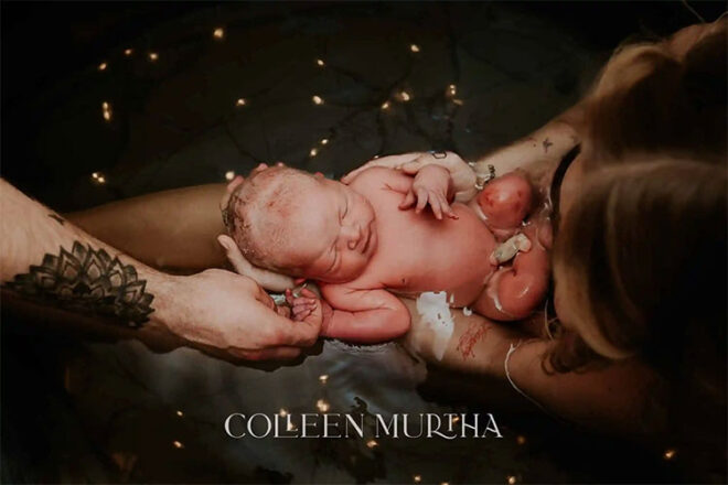 A newborn baby being cradled by two sets of hands surrounded by fairy lights