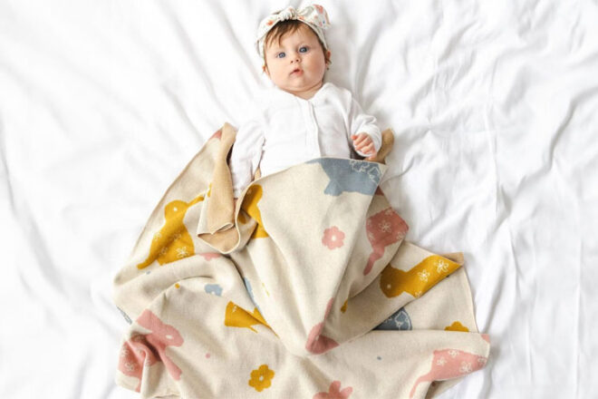 A baby laying on a bed covered in the Di Lusso Bunny Baby Blanket