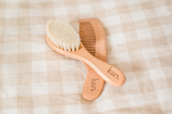 Kiin Wooden Baby Brush + Comb Set laying on a gingham bed spread