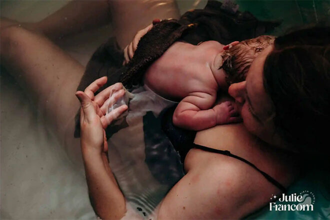 A woman laying in water with her newborn baby on her chest