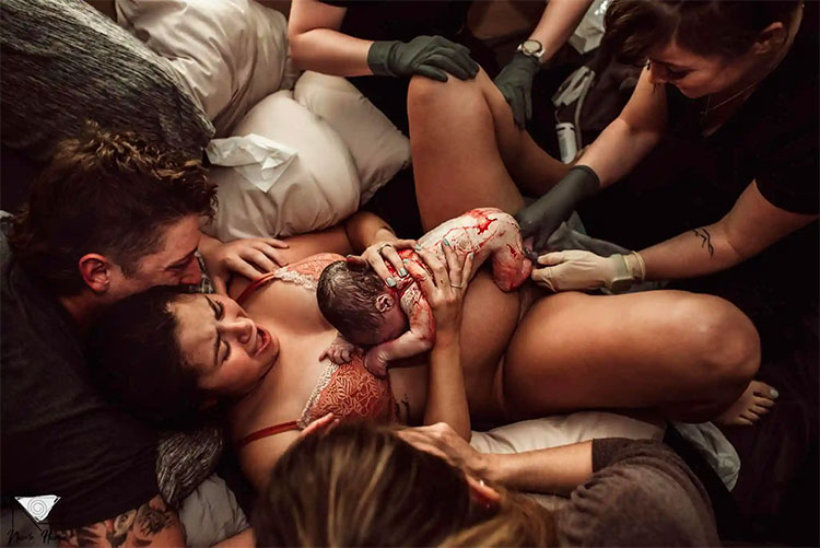 A woman with her newborn baby surrounded by people after giving birth