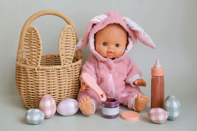 A baby doll surrounded by Easter paraphernalia and with the Tiny Harlow Easter Gift Set accessories