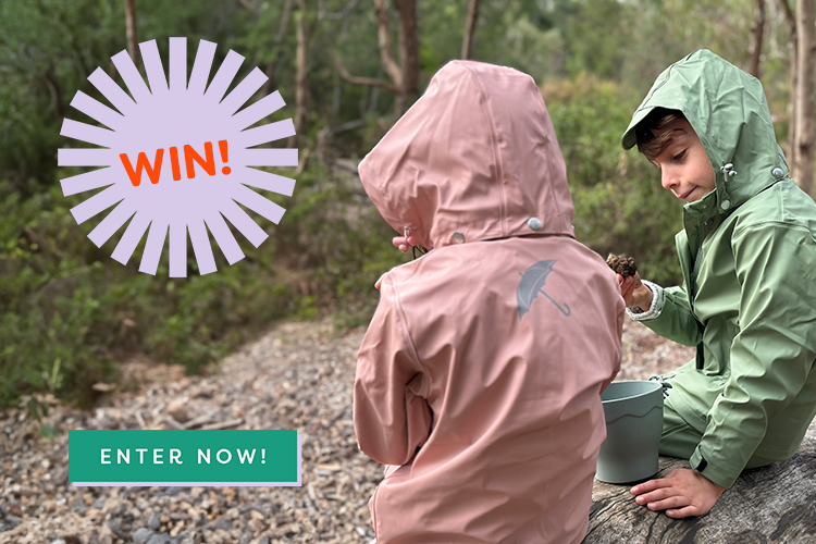 Two young children sitting on a log in Brolly Sheets wet weather gear with the words 'Win' and 'Enter Here'