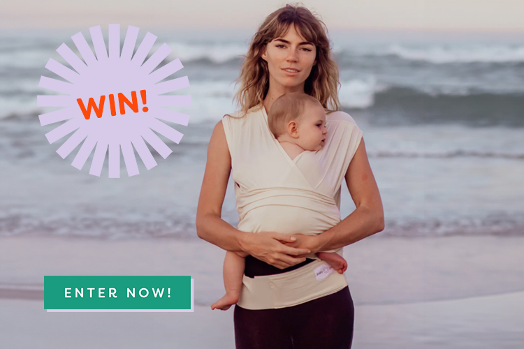 woman wearing a BabyDink newborn carrier on the beach with her baby.