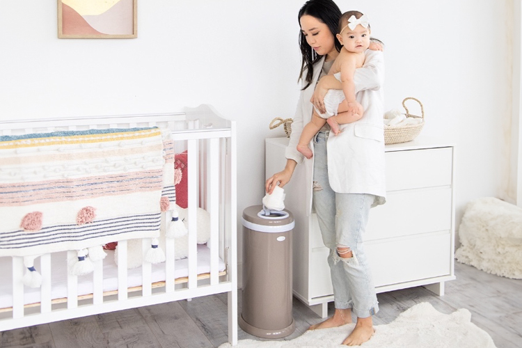 Mother holding baby putting a nappy into a Ubbi Nappy Bin