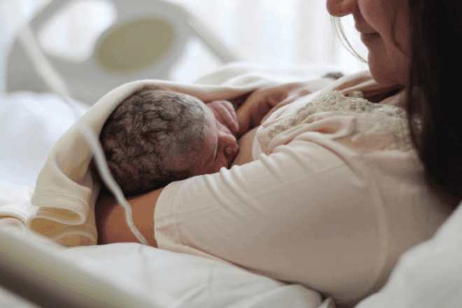 Mother holding and breastfeeding her newborn baby wrapped in a white blanket in hospital