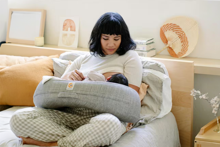 Mother breastfeeding her newborn baby using an Ergobaby nursing pillow to support latch